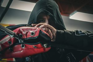 Close-up of hands adjusting red boxing equipment in dramatic lighting.