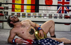Exhausted athlete lying on boxing ring floor draped in American flag with championship belt.