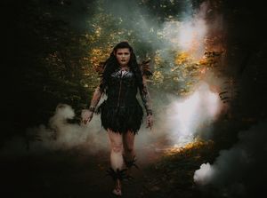 A dramatic forest photoshoot scene with dark smoke effects and moody lighting.