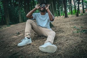 A joyful person lies on forest ground wearing casual clothes and white sneakers.