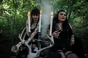 Gothic scene with lit candles and antlers in a dark forest setting.