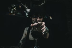 A dark atmospheric shot of someone holding a wine glass in dim lighting.