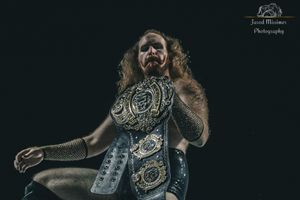 A performer in a sparkly dress dances energetically on a dark stage.
