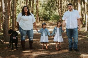Family members in casual white and denim outfits stand together in a wooded forest setting during an outdoor photo session.