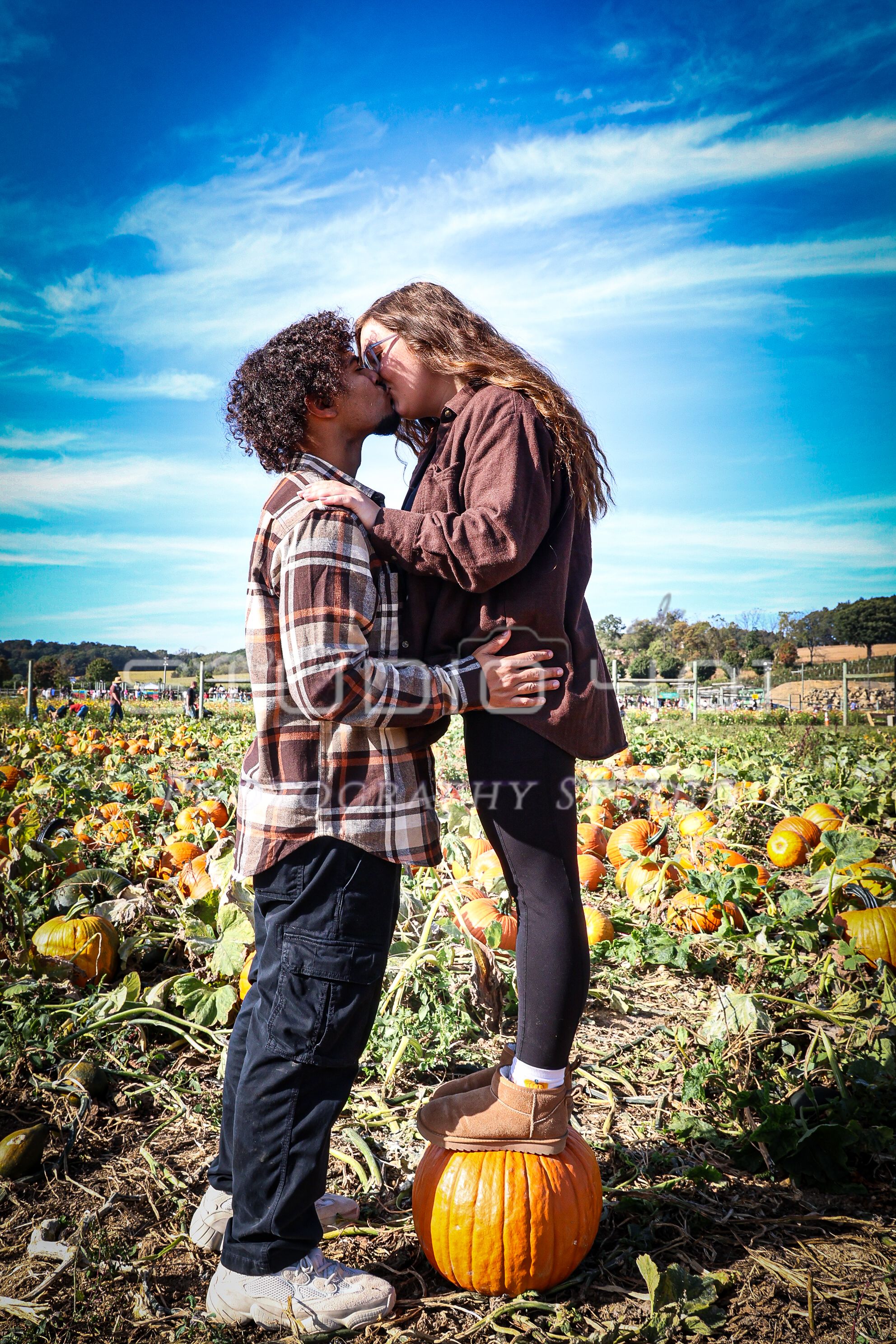 A romantic autumn moment shared between two people standing in a pumpkin patch under vibrant blue skies.
