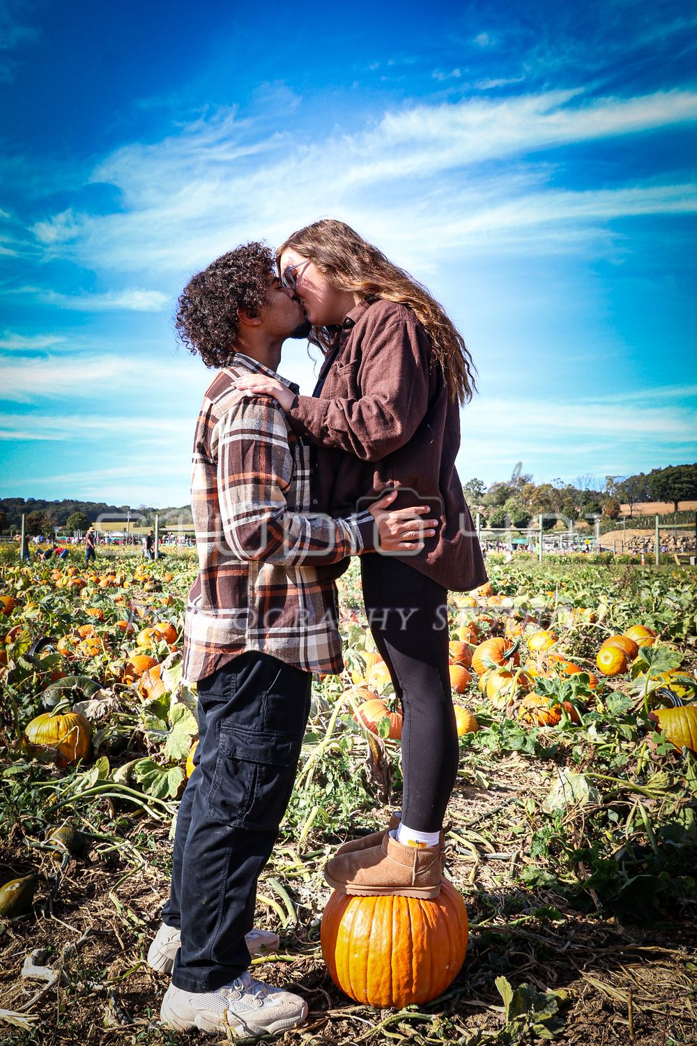 A romantic autumn moment shared between two people standing in a pumpkin patch under vibrant blue skies.