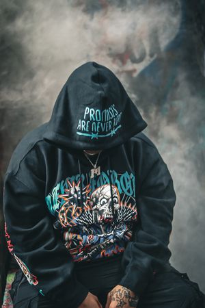 Black hoodie with urban street art design shown from behind in moody lighting with smoke effects.