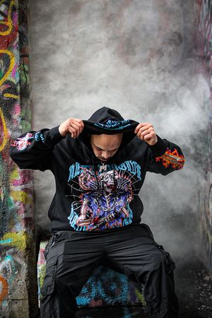 Person showing off details of street art hoodie design against graffiti backdrop.