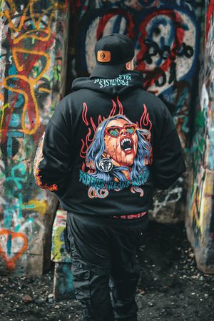 Back view of black hoodie featuring artistic design photographed against graffiti wall.