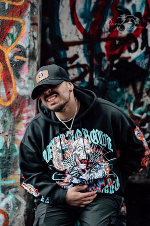Urban fashion shoot of black hoodie with blue graphic design against graffiti background.