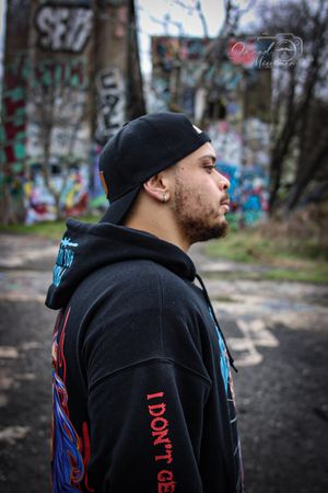 Profile view of streetwear fashion against urban graffiti backdrop with natural lighting.