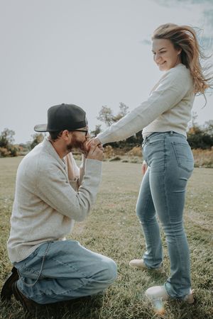 A couple shares an intimate moment outdoors in a grassy field wearing casual jeans and sweaters.