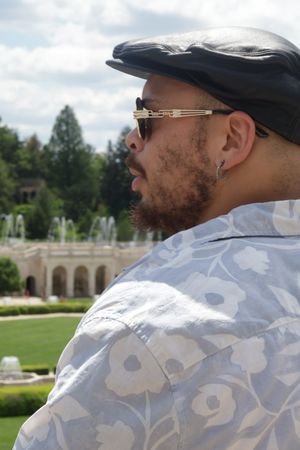 Person wearing camo pattern jacket and cap poses in sunny outdoor garden setting.