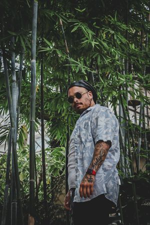 Person in sunglasses and light jacket posing against bamboo garden backdrop.