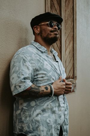 Someone in a light camo button-up shirt and cap posing against a beige wall.