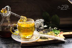 Golden herbal tea service with honey, citrus and herbs arranged on dark surface.