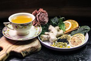 Artistic tea presentation with pink flowers, citrus and vintage cups on dark background.