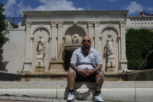 Person seated on bench in front of classic stone architecture with decorative statues.