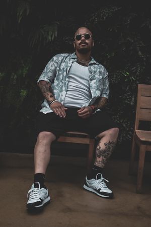 Person in camo shirt and sunglasses relaxing on wooden bench with sneakers visible.