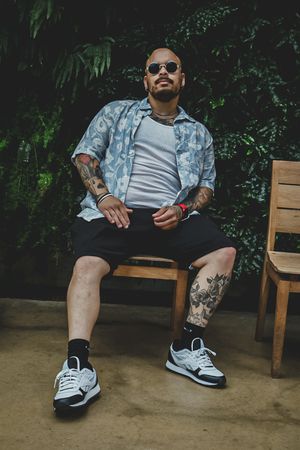 Someone sitting on wooden bench showing tattoos and wearing black and white sneakers.