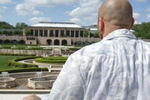 Person looking out over formal garden and historic mansion with manicured hedges and decorative landscaping.