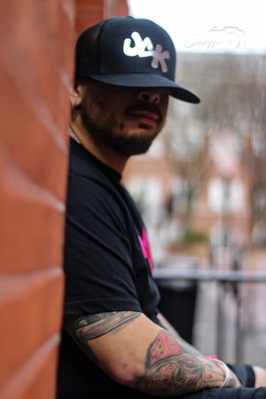 Close-up shots of person wearing black t-shirt with pink logo and baseball cap.