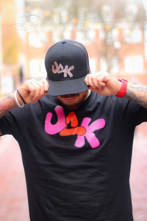 Person in black t-shirt with pink logo strikes pose with arms outstretched.