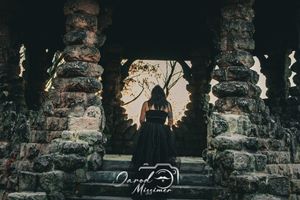A silhouetted figure stands between ancient stone pillars at dusk.