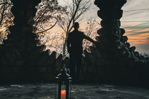 Dramatic silhouette against sunset through stone archway with lantern.
