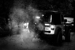 Black and white photo of a Jeep kicking up dust on a dirt trail.