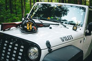 White Jeep Wrangler with firefighter helmet and gear mounted on hood.