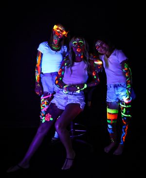 People in white shirts with fluorescent paint sitting together under UV lighting.
