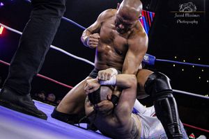 Professional wrestlers grappling in dramatic match under arena lights.