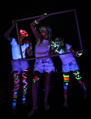 Performers sitting on a bar decorated with neon paint and glowing effects in dark room.