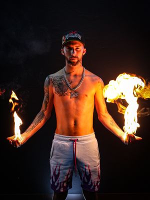 Fire performer creating dramatic display with dual flame props in darkness.