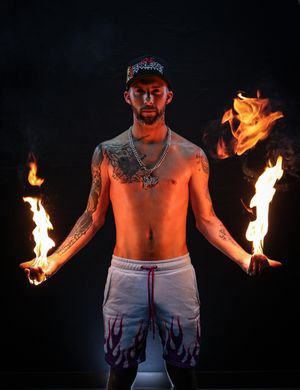 Fire artist wielding multiple flame props during nighttime performance.