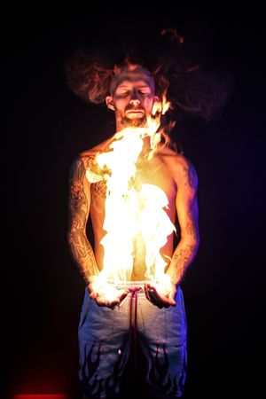 Fire breather creates spectacular flames against black background in artistic performance shots.