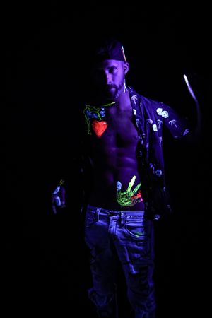 Blacklight photography reveals glowing neon designs on performer in dark setting.