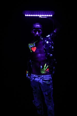 UV-reactive body decorations glow under purple lighting in artistic photography.