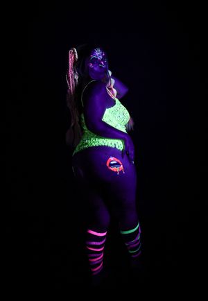 Figure in glowing neon bodysuit and paint posing under blacklight.