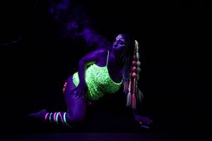 Person wearing fluorescent clothing glowing under UV lights in dark setting.