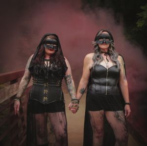 Two people in black leather outfits pose dramatically against a dark background.