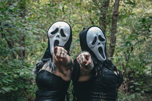 People in ghost masks pose playfully in a green forest setting.