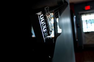 Close-up shot of a black electric guitar bridge and strings in low light.
