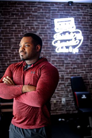 Person in burgundy sweater posed against brick wall with neon artwork.
