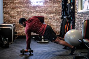 Athletic person performing plank exercise with dumbbells in a gym with brick wall background.