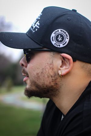 Side profile views of person wearing black baseball cap with brand logo in outdoor setting.