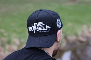 Detail shots of black baseball cap with white embroidered text against green background.