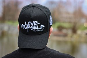 Multiple angles of black baseball cap with 'Love Yourself' branding in outdoor setting.