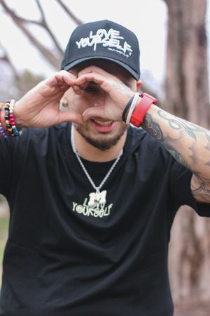 Person in black clothing and cap showing tattoos and jewelry in casual outdoor poses.